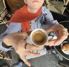 a woman is holding a cup of coffee in her right hand and wearing a red scarf around her neck