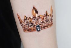 a close up of a person's arm with a gold crown tattoo on it