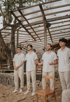 a group of men standing next to each other in front of a wooden structure on top of a beach