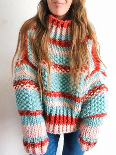 a woman with long hair wearing a colorful sweater and beanie is standing in front of a white wall