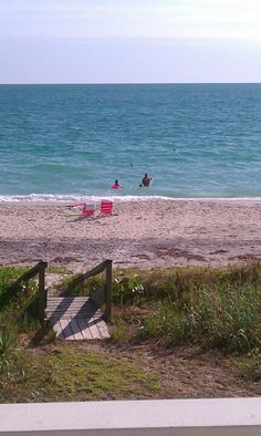 two people are sitting on the beach and one person is walking up to the water