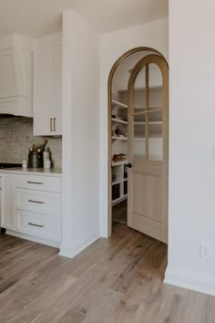 a kitchen with white cabinets and wood flooring next to an open door that leads to another room