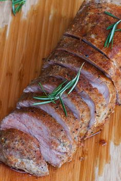 sliced meat sitting on top of a wooden cutting board with rosemary sprigs around it