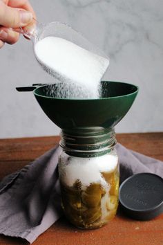 a person spooning sugar into a jar filled with pickles