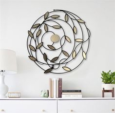 a metal wall sculpture with leaves and circles on the top, above a white dresser