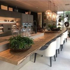 a dining room table that has some plants on it and lights hanging from the ceiling