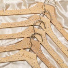 five wooden hangers with personalized names and pearls on them are laid out on a white satin surface