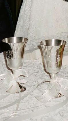 two silver wine goblets sitting on top of a white tablecloth covered table