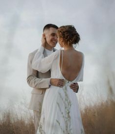 a man and woman standing next to each other in a field with tall dry grass