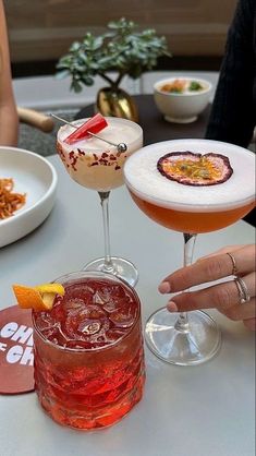 three cocktails are sitting on a table with plates and bowls in front of them