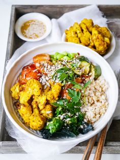 a white bowl filled with vegetables and rice next to chopsticks on a tray