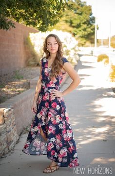 a woman in a floral dress poses on the sidewalk with her hands on her hips