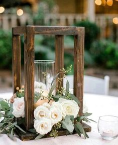 a wooden lantern with flowers and greenery sits on top of a table at a wedding reception