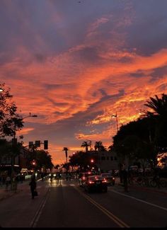 cars driving down the street in front of a colorful sky at dusk with clouds above