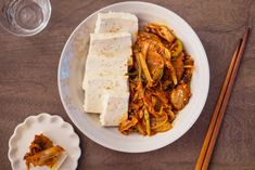 a bowl with noodles and tofu next to chopsticks on a wooden table