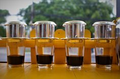 four shot glasses filled with liquid sitting on top of a wooden table next to a yellow bench