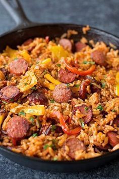 a skillet filled with rice and sausage on top of a table next to a fork