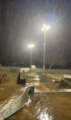 an empty skate park at night with the lights on and rain coming down all around