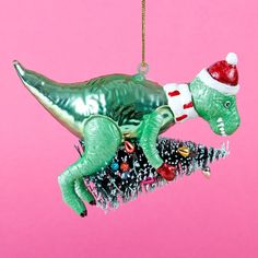 a green dinosaur ornament hanging from a pink background