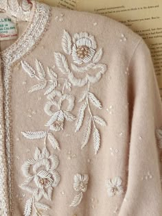 a pink sweater with white flowers on it sitting on top of an open book next to a pair of scissors