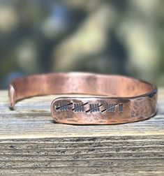 a close up of a metal bracelet on a wooden surface with trees in the background