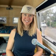 a woman wearing a hat and holding a microphone in front of a window with cars behind her