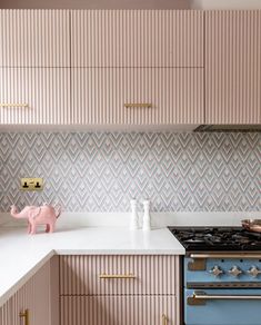 a kitchen with pink cabinets and white counter tops, an elephant figurine on the stove