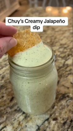 a hand holding a cracker over a jar filled with creamy jalapeno dip