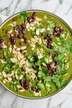 a pot filled with beans and greens on top of a marble countertop next to a spoon