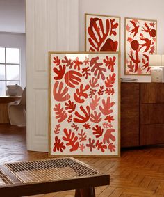 two red and white paintings on the wall next to a wooden table in a room