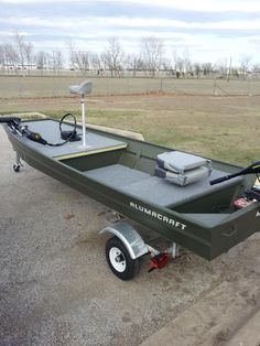 a green boat parked on the side of a road next to a field with an antenna