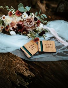 two wooden tags with names on them sitting next to a bouquet of flowers and veil