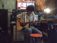 a young man sitting in front of a tv playing a guitar and singing into a microphone