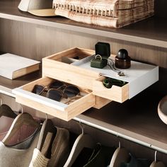 an open drawer in a closet filled with pairs of shoes and sunglasses on top of wooden shelves