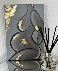 a glass vase filled with black and gold reeds next to a painting on a wall