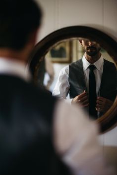 a man in a vest and tie is looking at himself in the mirror