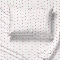 a bed with pink hearts on it and two pillows in the same color as the sheets