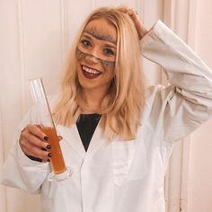 a woman in a white lab coat holding a glass with liquid on it and looking at the camera