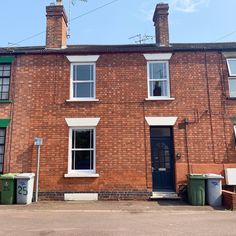 a brick building with two windows and trash cans outside