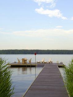 there is a dock that leads to the water and two lawn chairs are on it