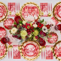 the table is set with red and white plates, silverware, and floral centerpieces