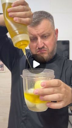 a man holding a cup filled with liquid and an orange in the other hand as he pours it into a jar