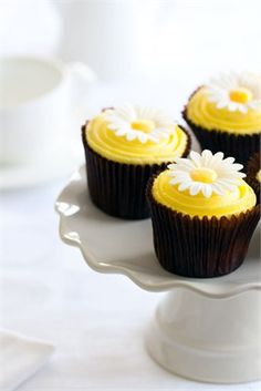 three cupcakes with yellow frosting and white flowers on top are sitting on a cake plate