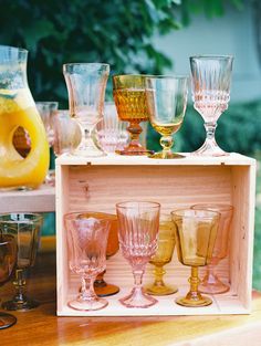 a wooden box filled with glasses on top of a table next to a yellow vase