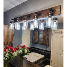 a bathroom vanity with mason jar lights and flowers on the counter top in front of it