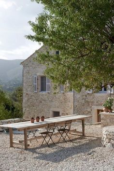 an outdoor table and chairs in front of a stone building with trees on the side