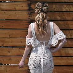 a woman standing in front of a wooden wall wearing a white crochet dress