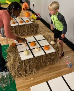 two children are playing checkers on hay bales with pumpkins in the background