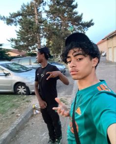 two young men standing next to each other on a street with cars parked in the background