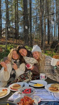 three women sitting at a picnic table with food and drinks in front of the camera